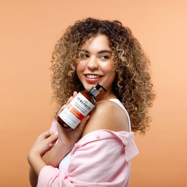 Woman with Curlsmith Essential Moisture Conditioner on an orange background