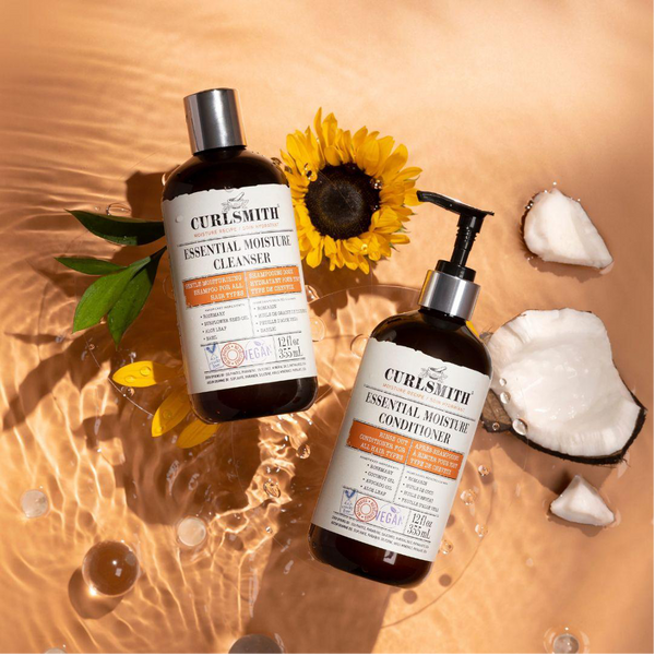 Two Curlsmith moisture products on an orange background with a sunflower and coconuts