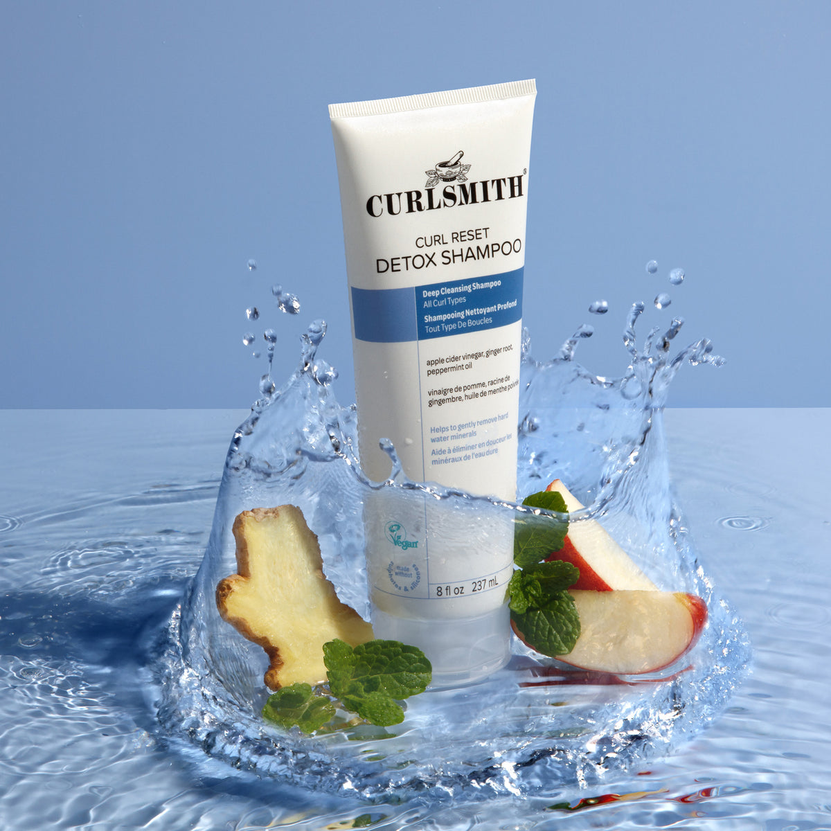 Curlsmith Curl Reset Detox Shampoo with apple slices and mint leaves on a water splash background