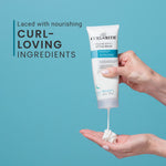 Hand holding a tube of CurlySmith Style Balm with blue background